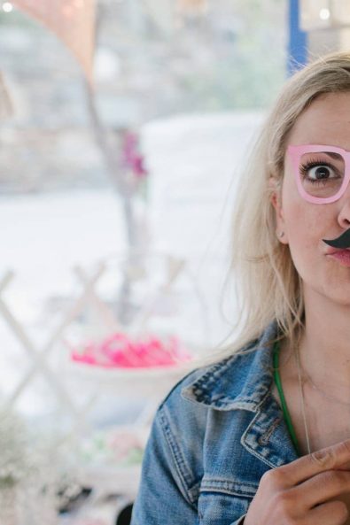 Beautiful blonde girl with photo booth props, pink glasses, and mustache.