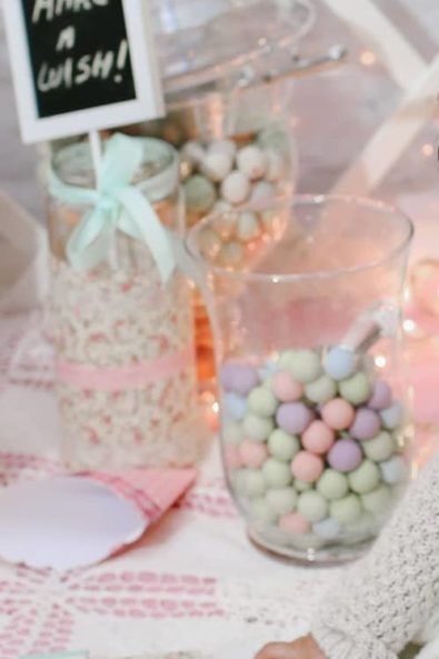 Baby girl in her crochet lace christening dress sitting on a candy bar with sweet treats playing with little chocolate crispy pops.