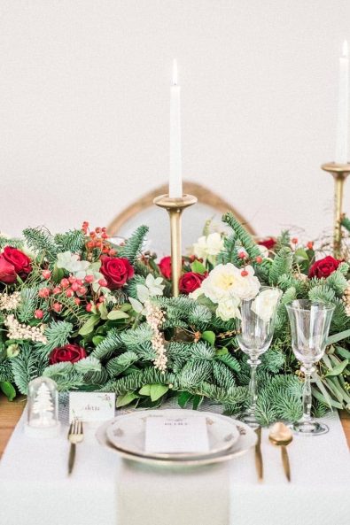 Christmas flowers table decoration with white candles, crystal glasses, and gold cutlery.