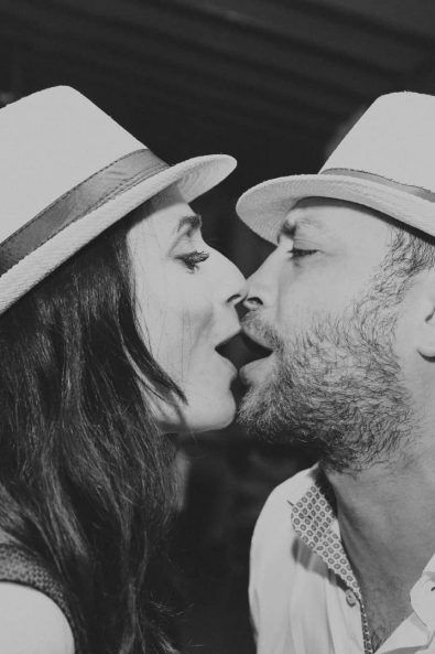 The mother and the father of the newly baptized baby dancing and kissing at their daughter's christening party reception while wearing raffia summer hats.