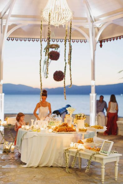 Dessert table candy bar table with white linen cloths, sweet treats and flower garlands.