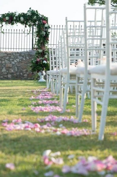Wedding venue with flower decorate altar and white wooden chairs and sprinkled pink rose petals on the grass.