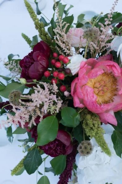 Moody and rich wedding flower arrangement with dark red peonies, hypericum berries, roses, and greenery.