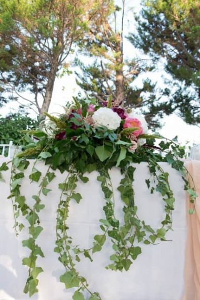 Bridal table flowers with vine and peonies and blush tablecloth.
