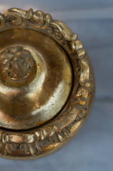 A decorative gold round box on a marble surface.