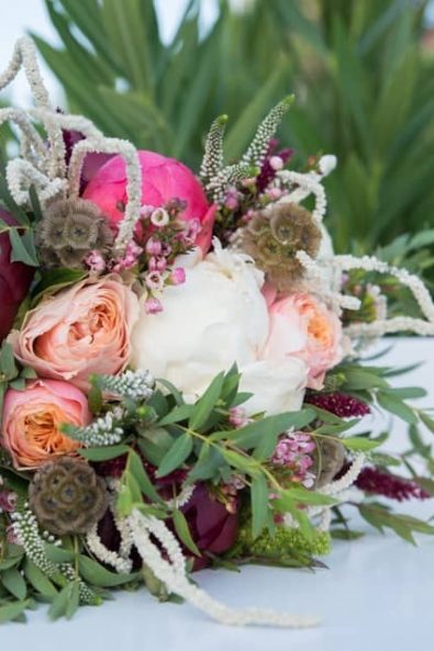 Spring wedding bouquet with blush and dark red peonies, greenery, and wildflowers.