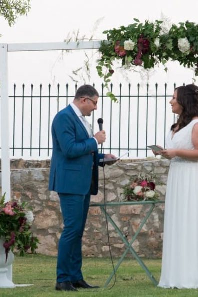 A couple exchanging vows in front of a flower decorated arch in an Athens estate garden wedding.