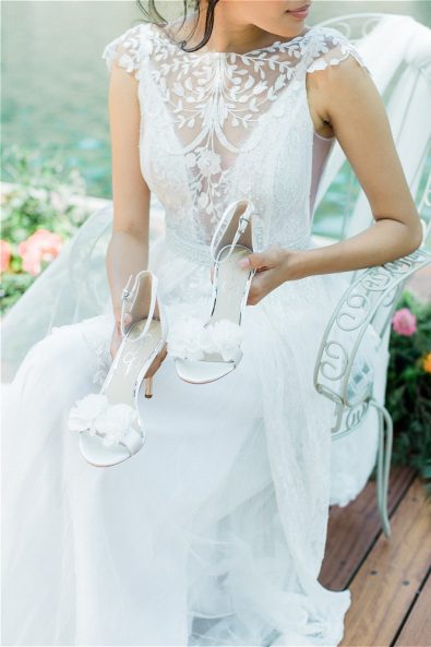 Bride in wedding gown holding white wedding heels