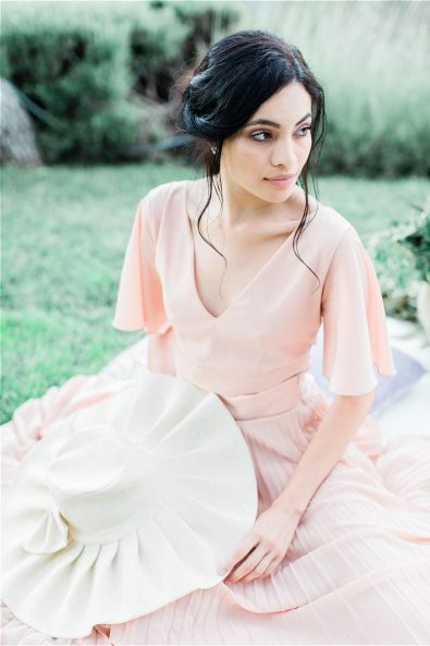 Bride stting down on grass holding a hat
