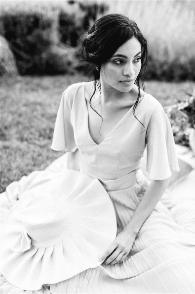 Black and White photo of bride stting down on grass holding a hat