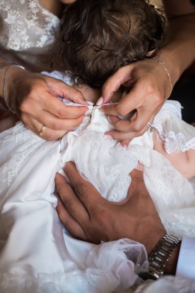 Close up shot of mother's and father's hand buttoning up their baby's white baby christening dress.