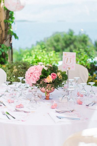 Pink and white table setting with custom made placemats, pink flower arrangement, macarons in a plexiglass box christening favors, crystal glasses, and silver flatware.