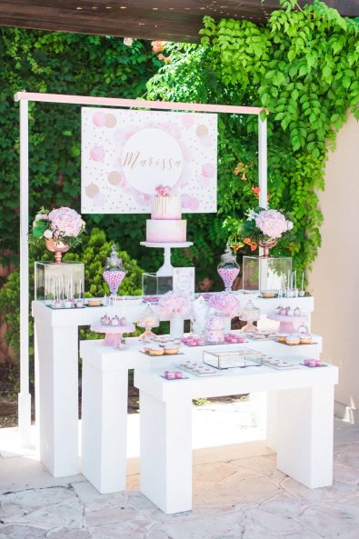 Shades of pink and rose gold inspired candy bar dessert table with macarons, donuts, cake pops, marshmallows and custom made sugar biscuits at a baby christening.