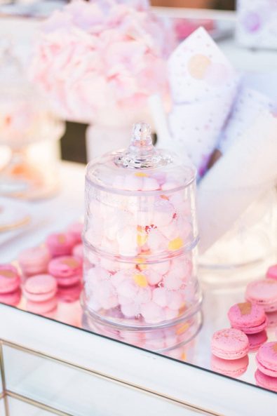 Crystal candy boxes with pink marshmallows on a mirrored tray with pink rose gold speckled macarons.