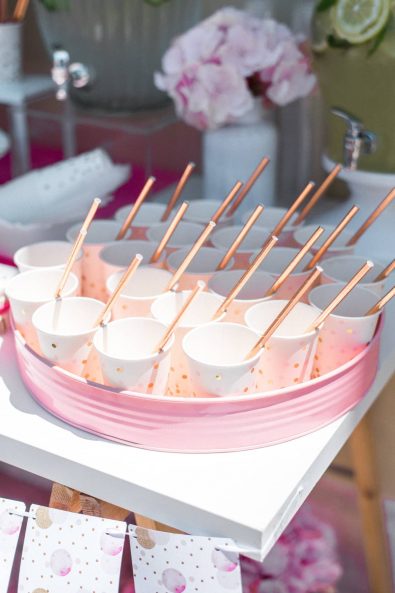 Close up shot of rose gold polka dot paper cups with rosegold straws on a refreshments stand for a christening day.