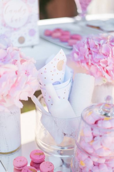 Close up shot of baptism candy bar with pink hydrangeas, confetti paper cones, and pink macarons.