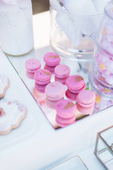 Vibrant pink gold speckled macarons on a mirrored tray for a christening candy bar.