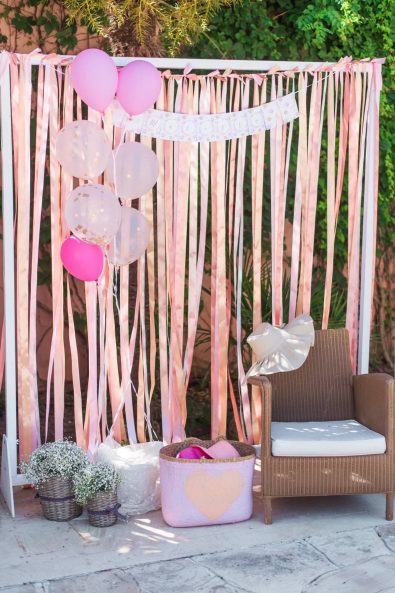 Peach and pink ribbons backdrop for a photo booth, colorful straw hats props and gold confetti balloons.