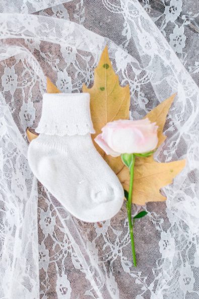 Shot of baby's tiny white sock and pink rose for a baby christening.