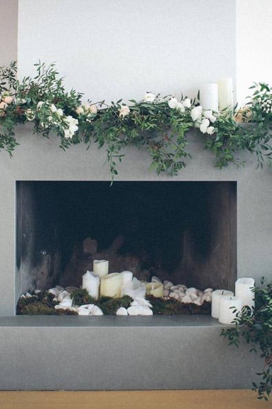 Concrete fireplace decorated with a wedding flower garland with roses, greenery and white flowers and white candles.