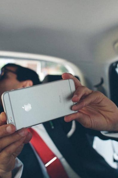 The bride and groom snapping selfies with an iPhone 6 at the back of their car.