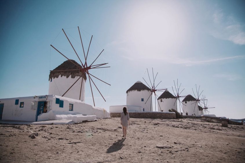 Woman walking in front of Mykonos windmillsdding in Greece, in front of the beach with chairs and the wedding aisle