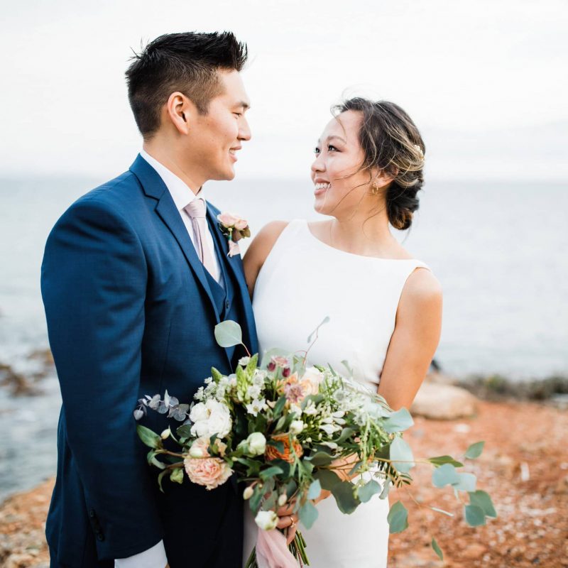 Bride with minimal wedding dress and organic flowers looking at her groom.