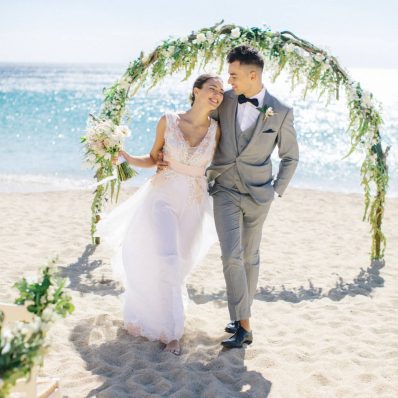 Happy couple leaving thew wedding arch at their beach wedding in Greece.