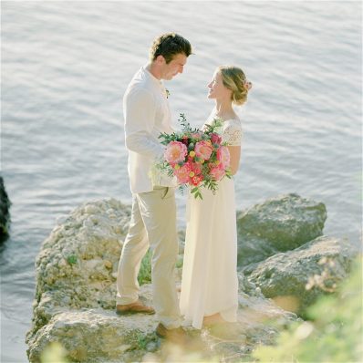 Bride and Groom stand on rock above the sea at their beach wedding
