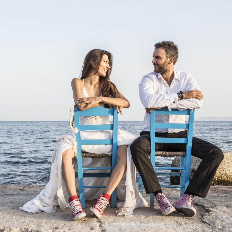 Groom and bride wearing converse all star shoes posing on two blue wooden chairs on The day of our wedding and christening.