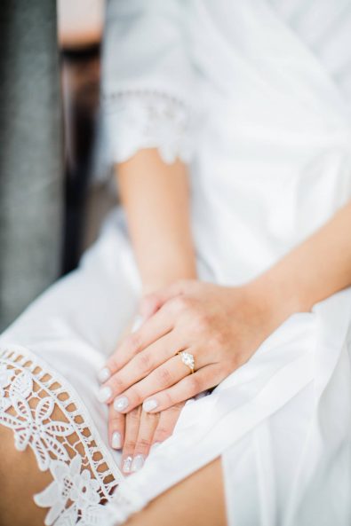 Close up shot of the bride's hand with bridal nude white manicure wearing her three stone diamond engagement ring.