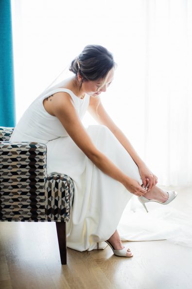 Elegant bride putting on her silver jimmy choo wedding shoes.