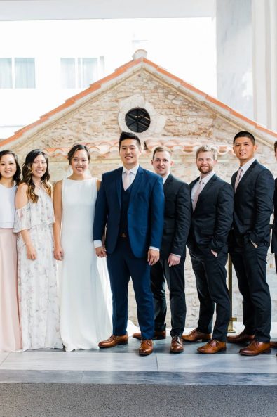 Group wedding photograph of bridesmaids, groomsmen, bride, and groom in a marble hotel entryway in Athens Greece.