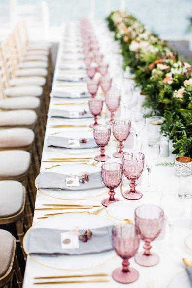 Fine art wedding table setting with gold flatware, gold-rimmed plates, berry glasses, grey linen napkins, and gold seal wax name tag for a destination wedding in Greece.