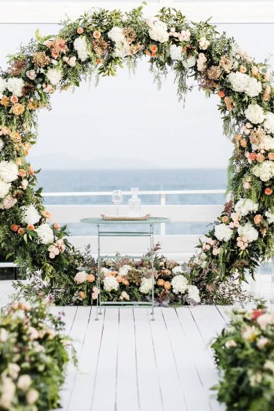 Contemporary flower decorated round arch and flower decorated aisle for a beachside wedding.
