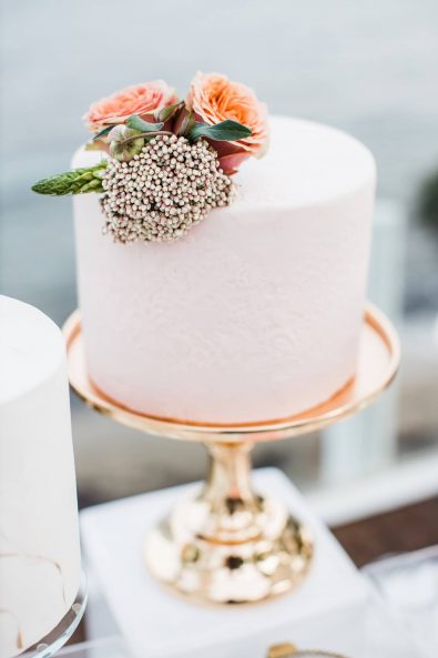 Light blush wedding cake with roses on a gold serving tray.