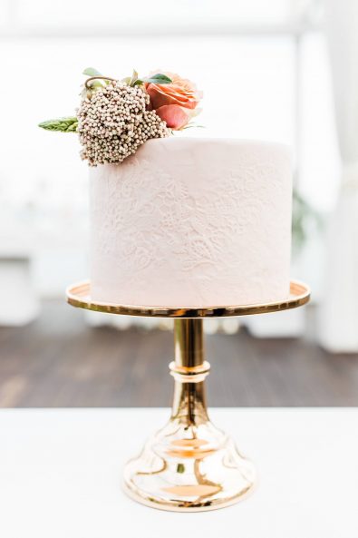 Lace imprint blush wedding cake with flower decorations on a gold serving tray.