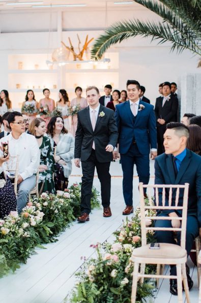 The groom and the best man walking down the aisle with guests looking at them.