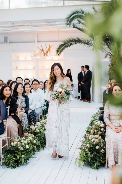 The maid of honor walking down the flower decorated aisle.