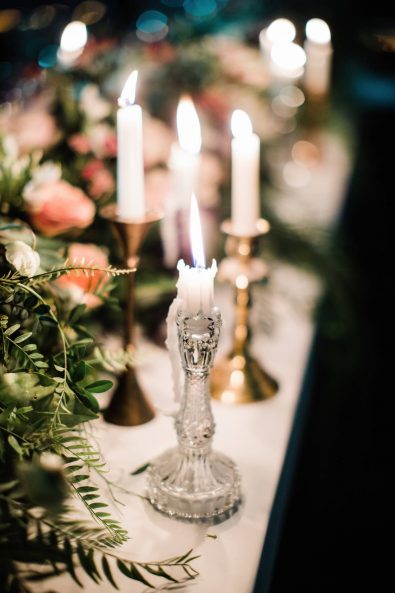 Close up shot of candleholders with melting candles on a table decorated with flowers.