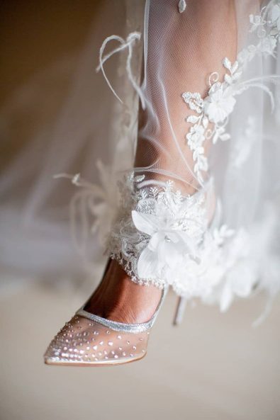 Detail shot of bride's lace and feathers wedding dress hemline and sparkly silver Louboutin shoes with Swarovski stones for a destination wedding in athenian riviera.