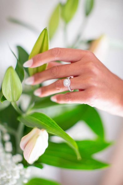 Detail shot of bride's hand with her diamond engagement ring and wedding manicure almond nude nails.