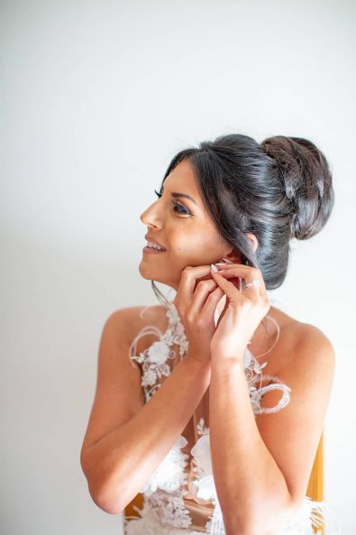 Shot of bride wearing her diamond stud earrings while wearing her sexy lace dress and bun hairstyle.