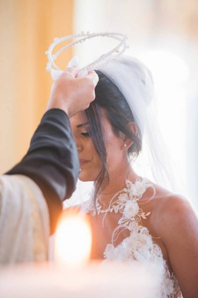 Portrait of the bride while the priest blesses the wedding crows on her forehead for a Greek Orthodox wedding ceremony in Greece.