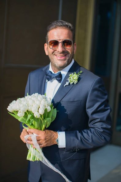 Groom holding the bridal bouquet with white tulips waiting for his bride to arrive.
