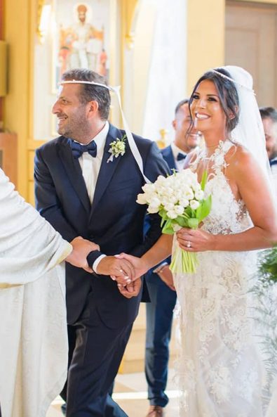 Bride and groom holding hands and priest holding the Gospel leading the way for the triple procession around the center table the