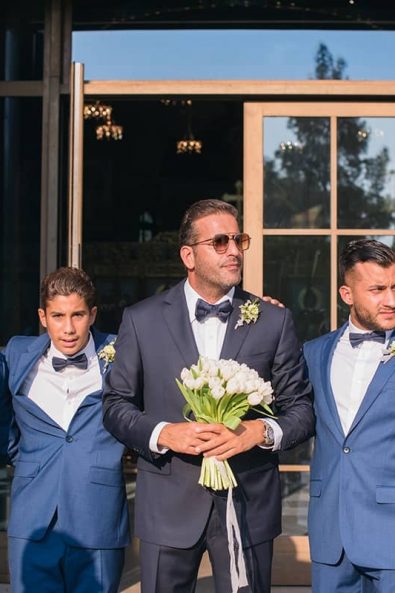 The groom and groomsmen wearing blue suits waiting for the bride to arrive in front of the church's entrance.