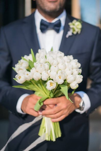 Close up shot of groom holding the minimal bridal bouquet with white tulips for a summer destination wedding in athenian riviera.