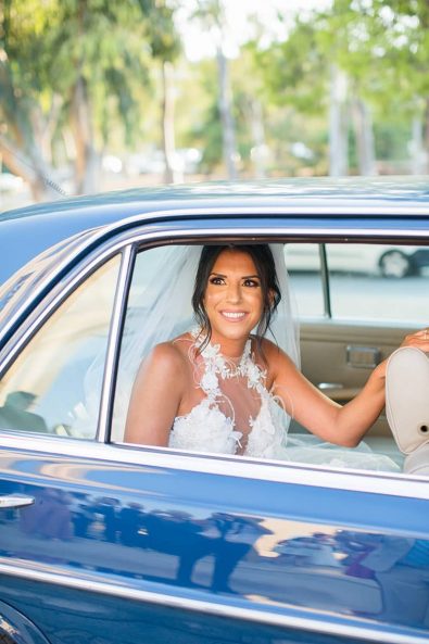 A smiling bride in a vintage blue car arriving at the church for her destination wedding in athenian riviera.