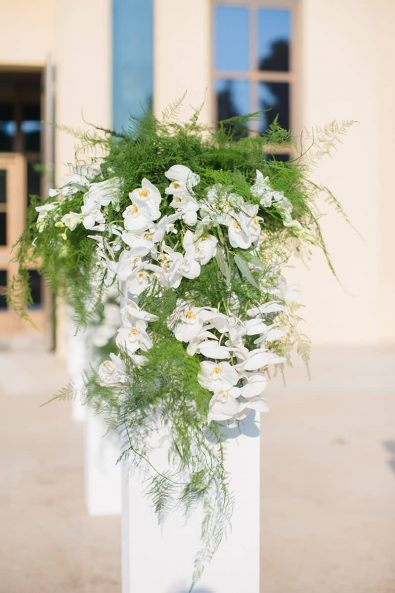 Flower stand entryway wedding floral decoration with white orchids and greenery.